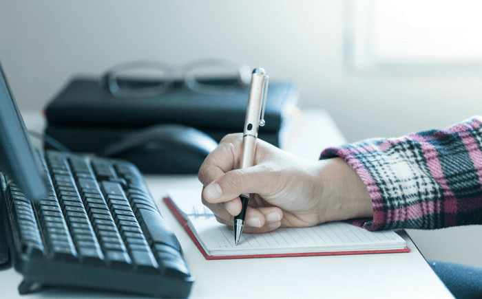 Hand with a pen starting to write next to a keyboard.